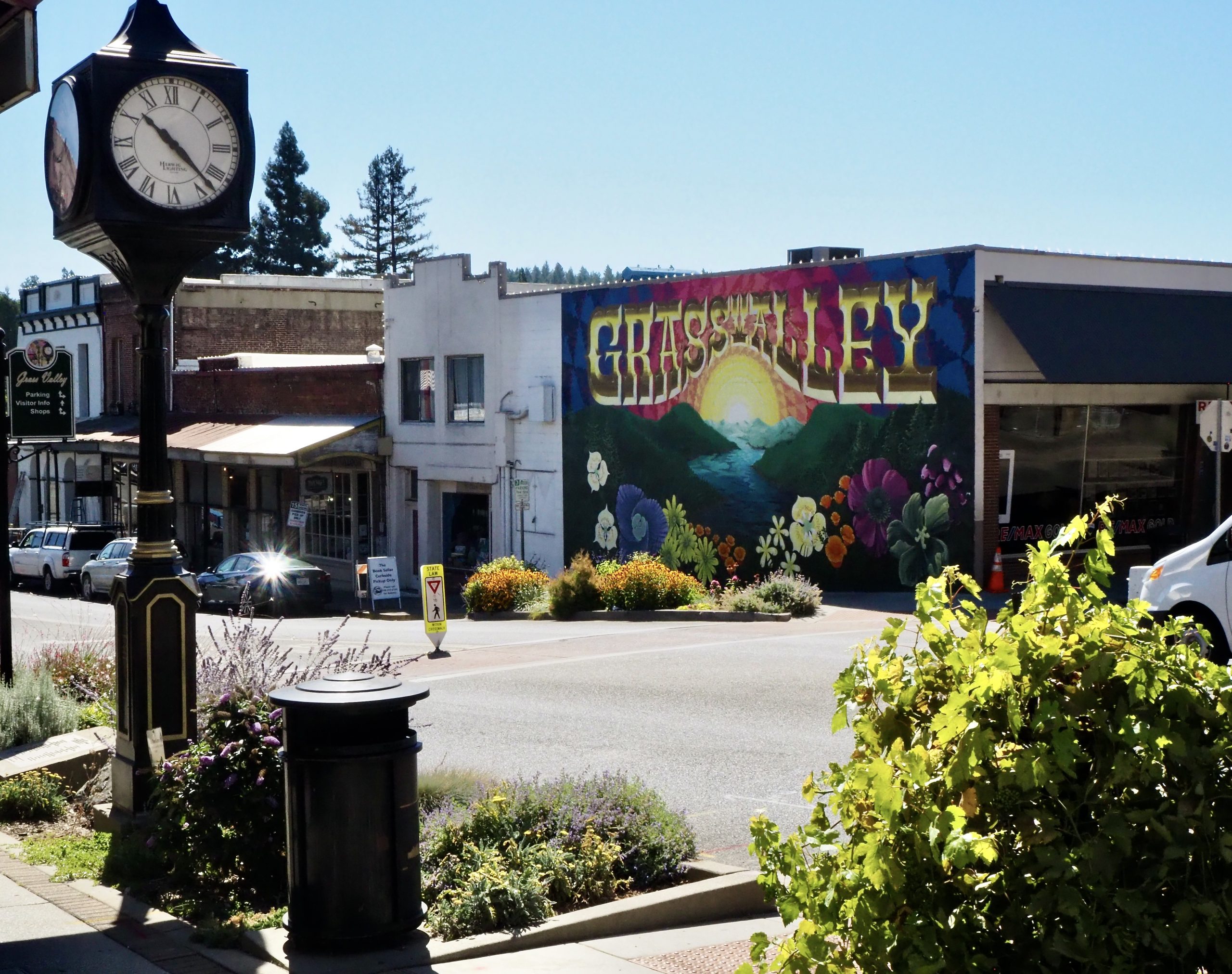 Colorful mural on E. Main Street in downtown Grass Valley, CA, featuring a scenic sunrise and floral artwork, with a historic clock in the foreground.