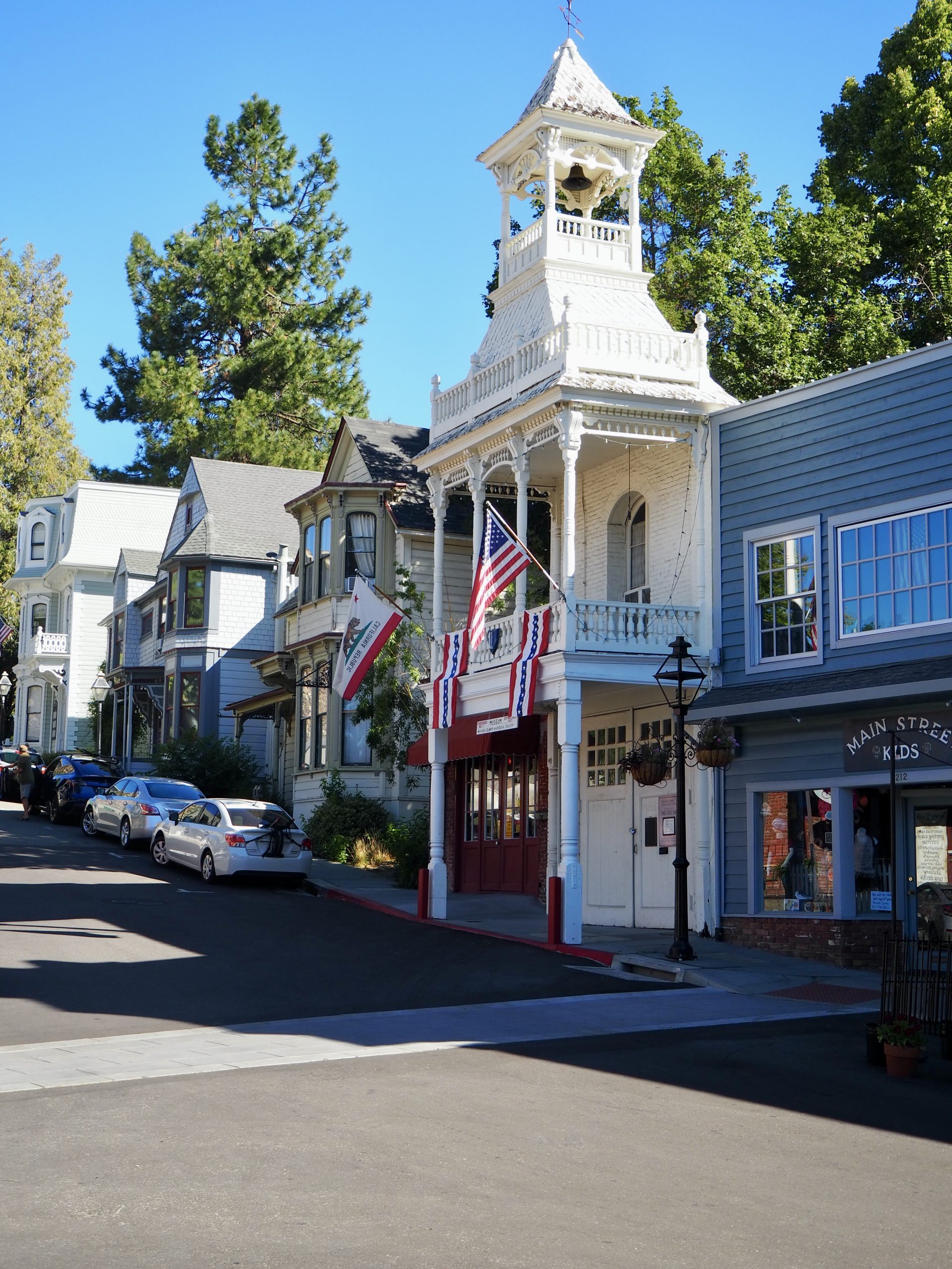 Historic Firehouse Museum in downtown Nevada City, CA, featuring Victorian architecture with patriotic decorations and nearby boutique shops.